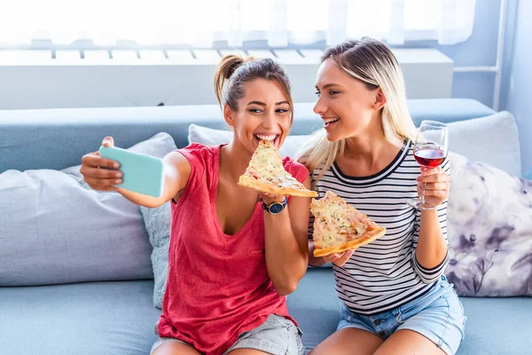 Friends eating pizza and smiling for selfie. They are sharing pizza and making selfie photo on mobile smart phone. They are having party at home, eating pizza and having fun.