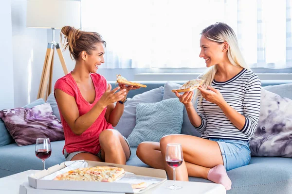 Two female friends chatting and enjoying eating pizza at home. Friends eating pizza.They are having party at home, eating pizza and having fun.
