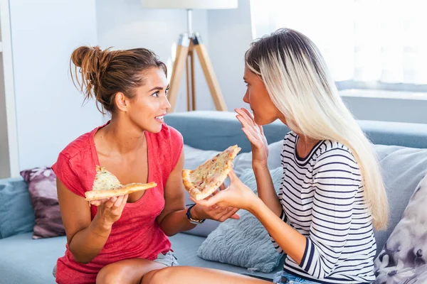 Two female friends chatting and enjoying eating pizza at home. Friends eating pizza.They are having party at home, eating pizza and having fun.