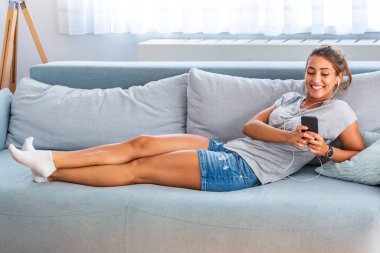Benim müzik ritmi rahatla. Çekici genç kadın lwith kulaklık ve evde koltukta oturan smartphone.