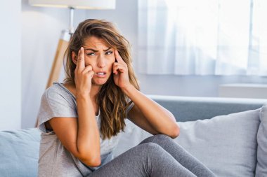 Çekici bir kadının portresi evde bir kanepede oturuyor, baş ağrısı çekiyor, acı çekiyor ve kendini kötü hissediyor..