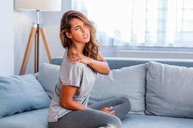 Omzum ağrıyor. Üst kol ağrısı, kas problemi, sağlık sigortası ve ilaç konsepti olan insanlar. Çekici bir kadın yatakta oturuyor ve başka bir elle ağrılı bir omuz tutuyor..