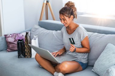 Güzel bir kadının kredi kartıyla alışveriş yaptığını gösteren bir fotoğraf. Kredi kartı tutan ve laptop kullanan bir kadın. Çevrimiçi alışveriş kavramı