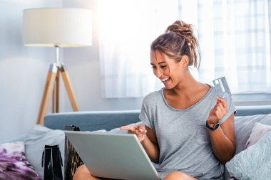 Genç bir kadın banka kartıyla internetten alışveriş yapıyor. Güzel kız evde online alışveriş için dizüstü bilgisayar kullanıyor.