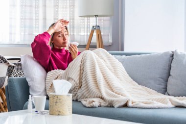 Soğuk algınlığı ve baş ağrısı olan bir kadın. Coronavirus belirtileri. Soğuk algınlığı veya COVID 19 'a yakalanmış genç bir kadın. Kanepede oturan, başı ağrıyan hasta kadın.