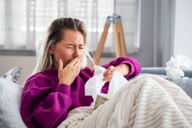 Hasta, çaresiz kadın grip olmuş. Rhinitis, soğuk, hastalık, alerji konsepti. Güzel hasta bir kadının burnu akıyor, burnu mendille sürtüyor. Hapşıran kadın. Esmer mendilin içinde hapşırıyor.
