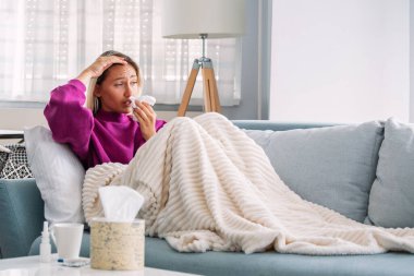 Hasta kadın. Flu. kadın üşüttü. Dokuların içine hapşırmak. Baş ağrısı. Virüs. İlaçlar. Burnunu mendile sümküren soğuk algınlığına yakalanmış genç bir kadın. Kanepede oturan, başı ağrıyan hasta kadın.