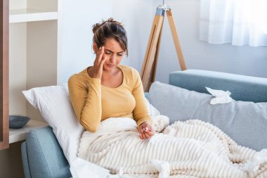 Hastalık, mevsimsel virüs problemi konsepti. Kanepede uzanmış, termometredeki sıcaklığa bakarak hasta olan bir kadın. Hasta kadın yüksek ateşle yatakta yatıyor. Soğuk algınlığı ve migren.