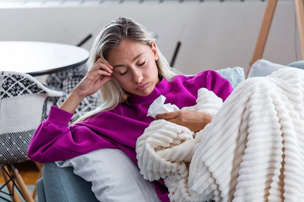 Sick woman with headache sitting under the blanket. Sick woman with seasonal infections, flu, allergy lying in bed. Sick woman covered with a blanket lying in bed with high fever and a flu, resting.