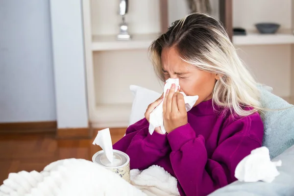 Sick Woman.Flu.Woman Caught Cold. Sneezing into Tissue. Headache. Virus .Medicines. Young Woman Infected With Cold Blowing Her Nose In Handkerchief. Sick woman with a headache sitting on a sofa