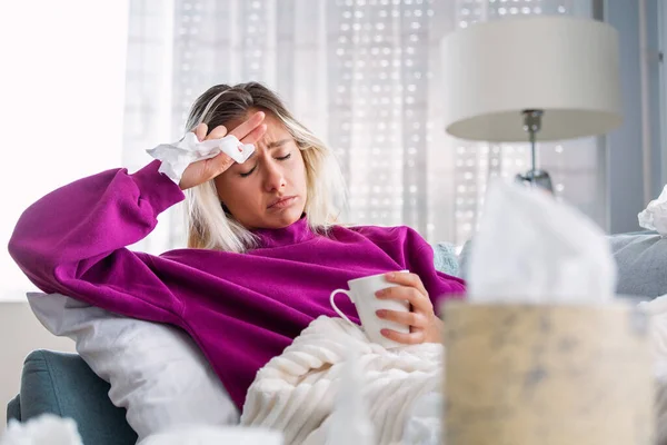 生病的女人 女人感冒了 在组织里打喷嚏头疼 年轻女子被冷吹鼻涕感染在手巾上 一个头痛的生病女人坐在沙发上 — 图库照片