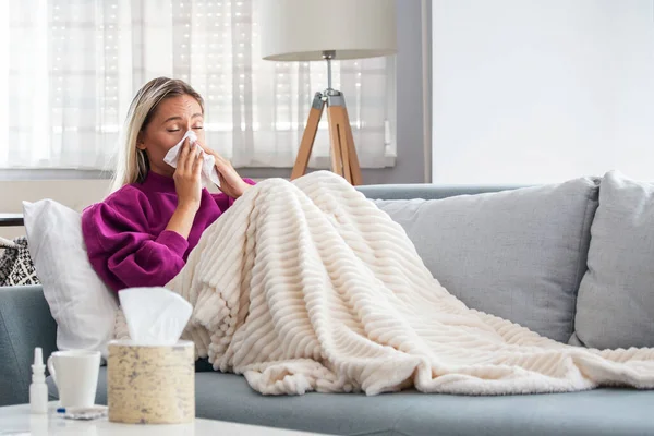 Sick woman with headache sitting under the blanket. Sick woman with seasonal infections, flu, allergy lying in bed. Sick woman covered with a blanket lying in bed with high fever and a flu, resting.