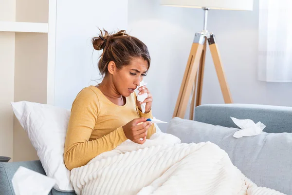 季節のウイルス問題の概念 風邪をひいた女性は温度計で温度を見てソファに寝そべっている 病気の女性が高熱でベッドに横たわっている 風邪インフルエンザと片頭痛 — ストック写真