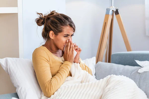 生病的女人 女人感冒了 在组织里打喷嚏头疼 年轻女子被冷吹鼻涕感染在手巾上 一个头痛的生病女人坐在沙发上 — 图库照片
