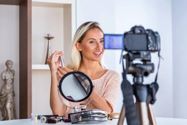 Young lady talking on cosmetics holding a makeup palette while recording her video. Woman making a video for her blog on cosmetics.