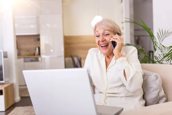 Senior woman receiving good news on phone. screaming out of happiness. Mature excited woman screaming in happiness while talking on a phone and using laptop
