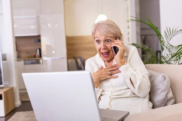 Senior woman receiving good news on phone. screaming out of happiness. Mature excited woman screaming in happiness while talking on a phone and using laptop