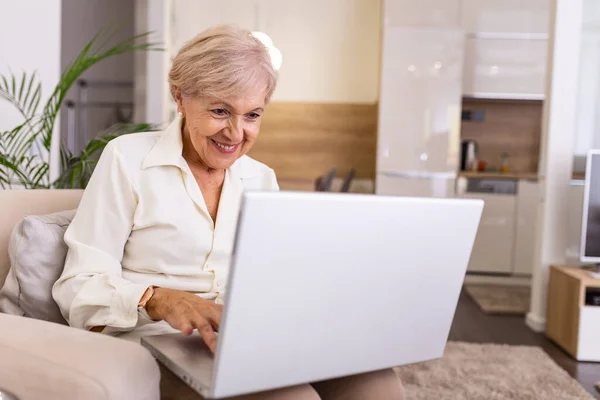 Elderly lady working with laptop. Portrait of beautiful older woman working laptop computer indoors. Senior woman using laptop at home, laughing