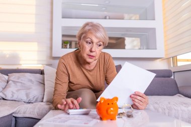 Yaşlı kadın aldığı faturalarla şok oldu, dehşete düştü ve nefes nefese kaldı. Kıdemli kadın evde hesap makinesiyle finansmanı kontrol ediyor. Emekli kadın ev faturalarını hesaplıyor.