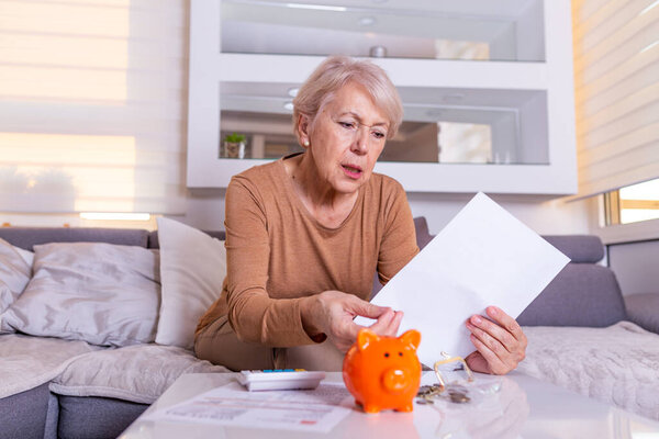 savings, money, annuity insurance, retirement and people concept - Senior woman hand putting coin into piggy bank. Senior old woman shocked with the bills she receives, appalled and gasping