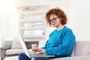 Positive young woman freelancer watching video in blog on netbook and having a coffee at comfortable home. Beautiful young business woman working on laptop.Freelancer connecting to internet
