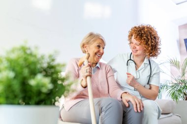 Friendly relationship between smiling caregiver in uniform and happy elderly woman. Supportive young nurse looking at senior woman. Young caring lovely caregiver and happy ward clipart