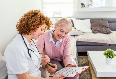 Senior woman is visited by her doctor or caregiver. Female doctor or nurse talking with senior patient. Medicine, age, health care and home care concept. Senior woman with her caregiver at home