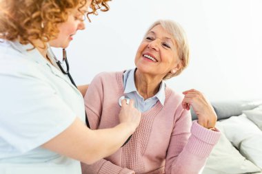 Ev ziyareti sırasında sağlık ziyaretçisi ve yaşlı bir kadın. Genç bayan doktor kıdemli hastayı muayene ediyor. Beyaz önlüklü genç bayan doktor kıdemli kadını muayene ediyor..