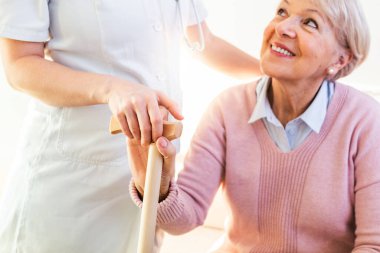 Yaşlı bir kadının eline dokunan kişiye yakın çekim. Ev yardımı kavramı. Huzurevinde genç bakıcıların el ele tutuşan yaşlı kadın. Geriatrik doktor ya da yaşlılar konsepti..