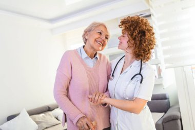 Genç bakıcı, yaşlı engelli kadını bastonla destekliyor. Mutlu kadın bakıcı portresi ve evde birlikte yürüyen son sınıf öğrencisi. Profesyonel bakıcı yaşlı bir kadınla ilgileniyor..