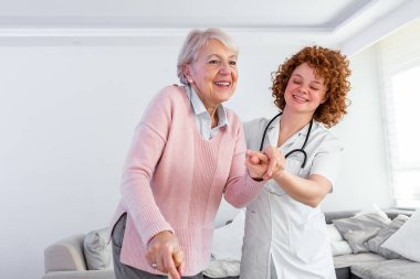Gülümseyen hemşire huzurevinde dolaşmasına yardım ediyor. Mutlu kadın bakıcı portresi ve evde birlikte yürüyen son sınıf öğrencisi. Profesyonel bakıcı yaşlı bir kadınla ilgileniyor..
