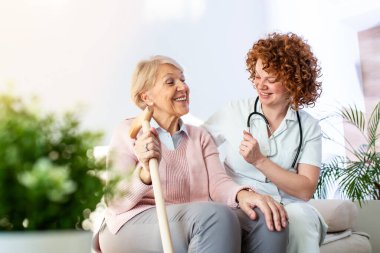 Friendly relationship between smiling caregiver in uniform and happy elderly woman. Supportive young nurse looking at senior woman. Young caring lovely caregiver and happy ward