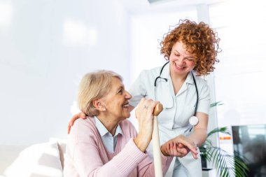 Friendly relationship between smiling caregiver in uniform and happy elderly woman. Supportive young nurse looking at senior woman. Young caring lovely caregiver and happy ward