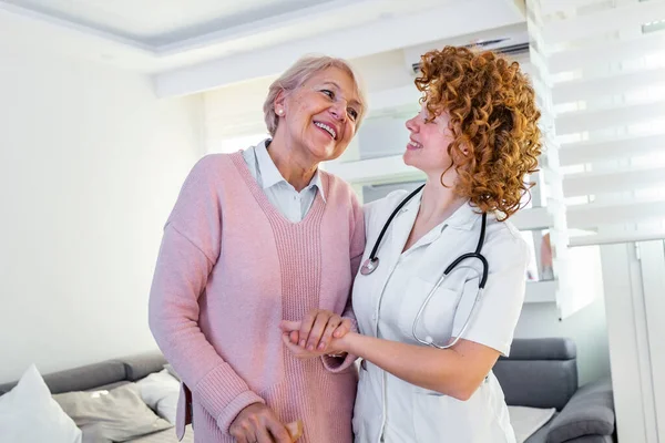 Gülümseyen hemşire huzurevinde dolaşmasına yardım ediyor. Mutlu kadın bakıcı portresi ve evde birlikte yürüyen son sınıf öğrencisi. Profesyonel bakıcı yaşlı bir kadınla ilgileniyor..