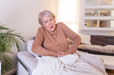 Yaşlılık, sağlık sorunları ve insanların konsepti - evde karın ağrısı çeken son sınıf öğrencisi kadın. Evde karın ağrısı çeken yaşlı bir kadın.