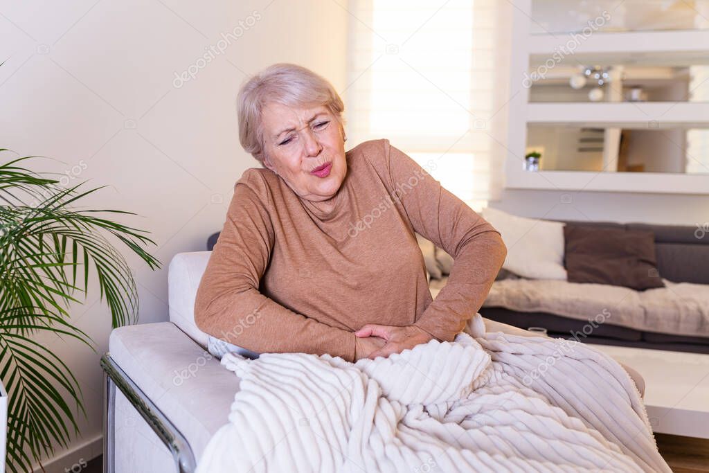 Old age, health problem and people concept - senior woman suffering from stomach ache at home. Senior woman suffering from stomach pain at home