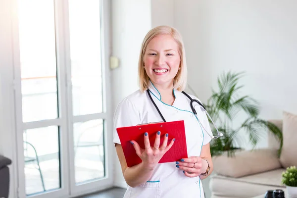 Female doctor holding clip board and smiling. Woman doctor standing straight in home care hospital. Close-up of a female doctor using clip board with stethoscope around her neck