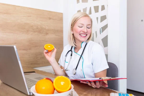 Χαμογελώντας Διατροφολόγος Στο Γραφείο Της Κρατά Ένα Φρούτο Και Δείχνει — Φωτογραφία Αρχείου