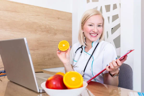 Smiling nutritionist in her office, she is showing healthy vegetables and fruits, healthcare and diet concept. Female nutritionist with fruits working at her desk.