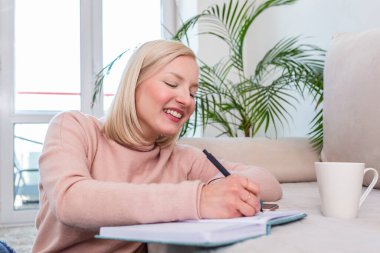 Sınavdan bir gün önce ders çalışan bir kız, kalemle notlar yazıyor. Güzel genç kız evde ders çalışıyor. Oturma odasında yerde oturmuş ders notlarını okuyor.