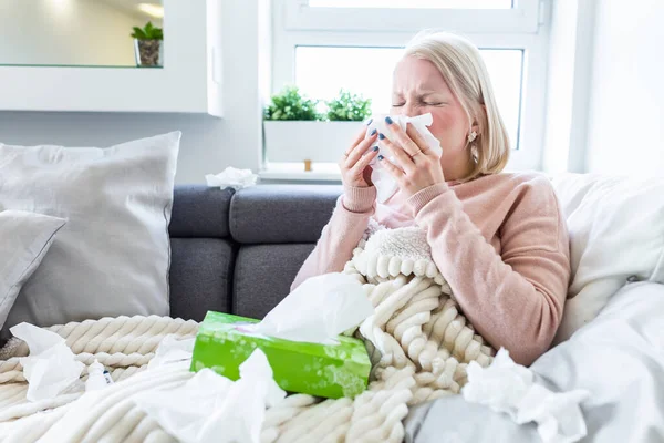 Sick Albino Woman.Flu.Woman Caught Cold. Sneezing into Tissue. Headache. Virus .Medicines. Young Woman Infected With Cold Blowing Her Nose In Handkerchief. Sick woman with a headache sitting on a sofa