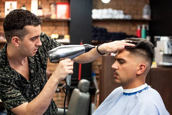 Close-up, master Barber does the hairstyle and styling with dryer, dries hair to guy. Concept Barbershop. Soft focus.