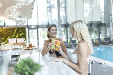 İki havalı, güzel, eğlenceli, mutlu, bronzlaşmış kadın kokteyl ile tatil köyünde yüzme havuzunun yanında