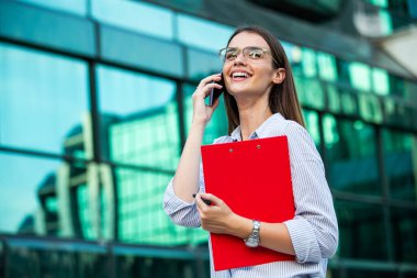 Cep telefonuyla konuşan güzel ve mutlu bir iş kadını. Başarılı İş Kadını 'nın portresi. Takım elbiseli ve elinde belgelerle fotoğrafçı kadın..