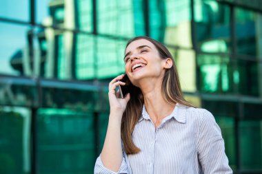 Ofis yakınında telefonu olan bir iş kadını. Moda içinde gülümseyen güzel bir kadının portresi. Ofis kıyafetleri dışarıda dururken telefonda konuşuyor. Telefon iletişimi. Yüksek Kalite Resim.