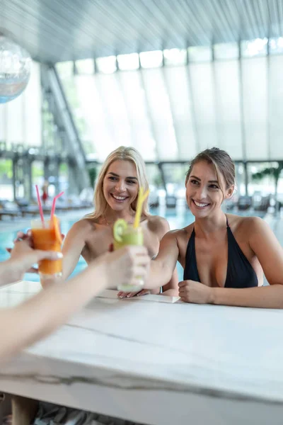 Two beautiful women relaxing at swimming pool with cocktails. Beautiful young women drinking cocktails in the swimming pool bar