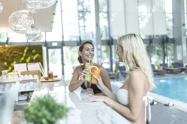 İki havalı, güzel, eğlenceli, mutlu, bronzlaşmış kadın kokteyl ile tatil köyünde yüzme havuzunun yanında