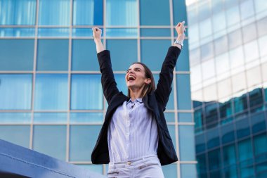 businesswoman in a business suit, exulted by happiness after finishing the deal, in the background skyscrapers. Concept of: business, technology, economy and work and success.