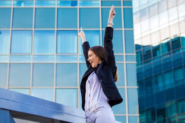 businesswoman in a business suit, exulted by happiness after finishing the deal, in the background skyscrapers. Concept of: business, technology, economy and work and success.