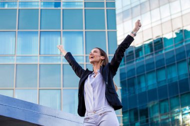 businesswoman in a business suit, exulted by happiness after finishing the deal, in the background skyscrapers. Concept of: business, technology, economy and work and success.